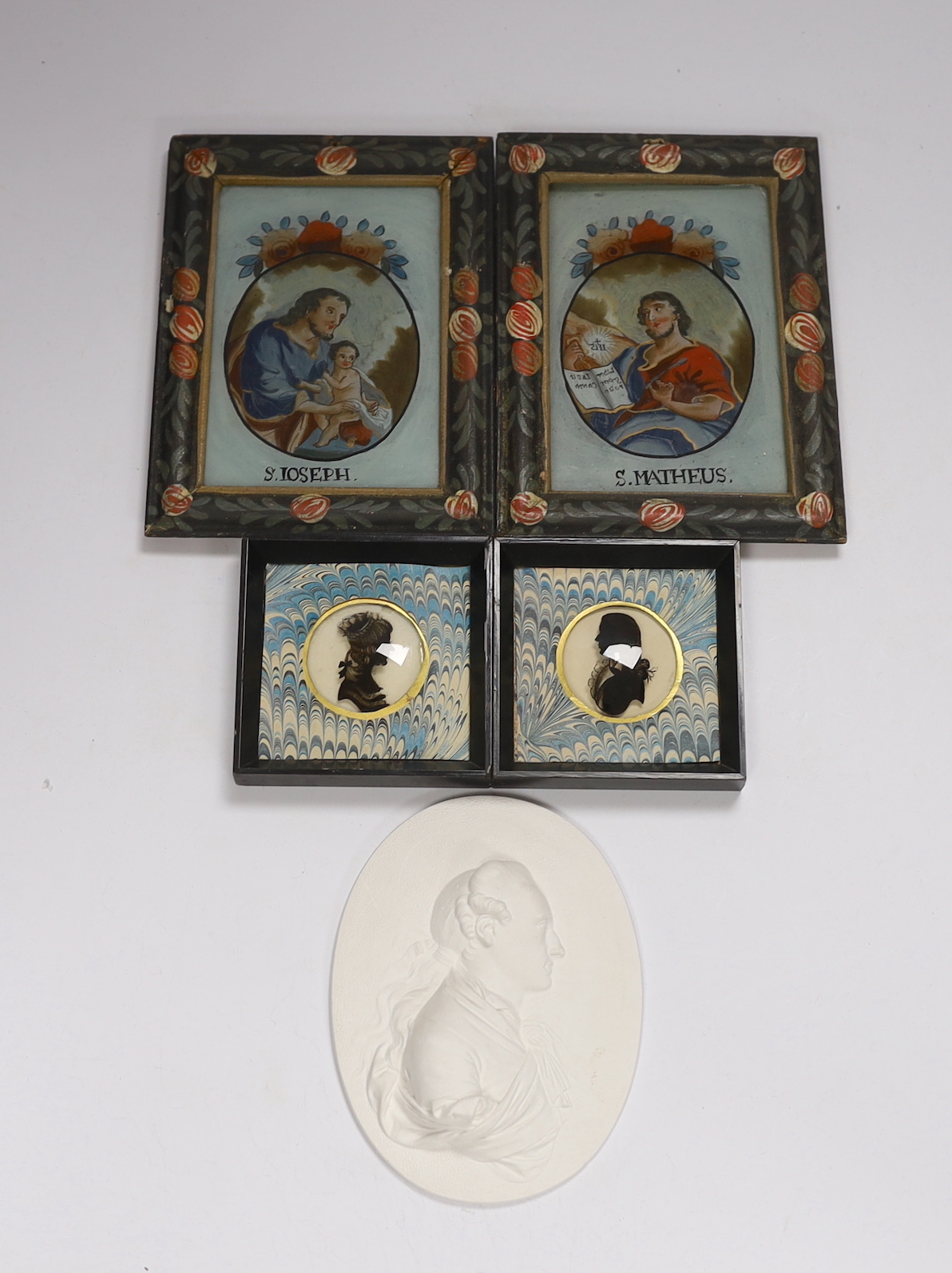 A pair of small reverse painted glass silhouettes, a pair of reverse painted glass panels of St Joseph and St Matheus and an oval plaster relief profile of a Regency gentleman, reverse paintings 14.5cm high x 9.5cm wide